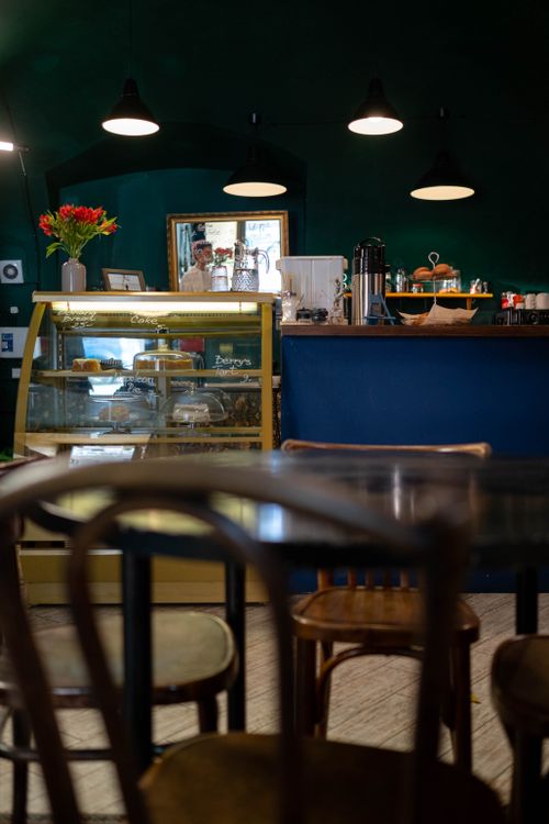 Free Warm café interior with wooden furniture, counter, and display case showcasing pastries. Stock Photo