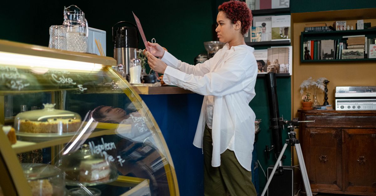 Uma mulher em um café olha para o menu enquanto está de pé ao lado do balcão, cercada por uma decoração aconchegante.