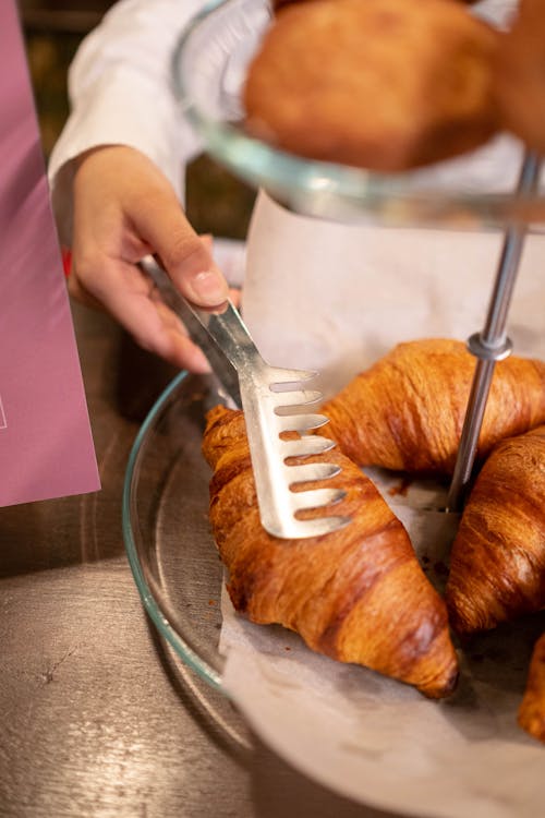 Close-Up Shot of a Person Holding a Croissant Using Tongs