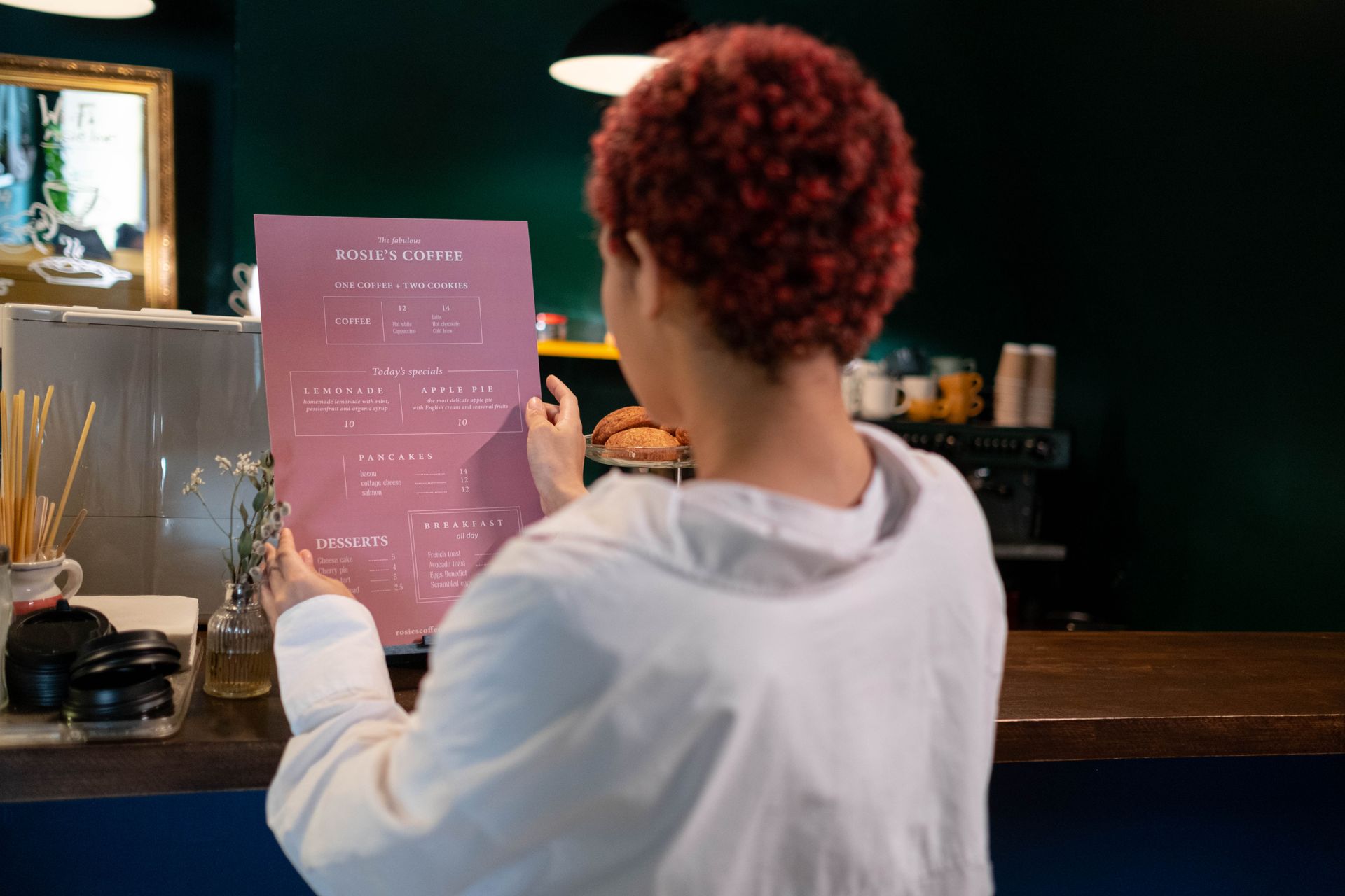 A woman with afro hair in a cafe, reading a menu with daily specials on offer.