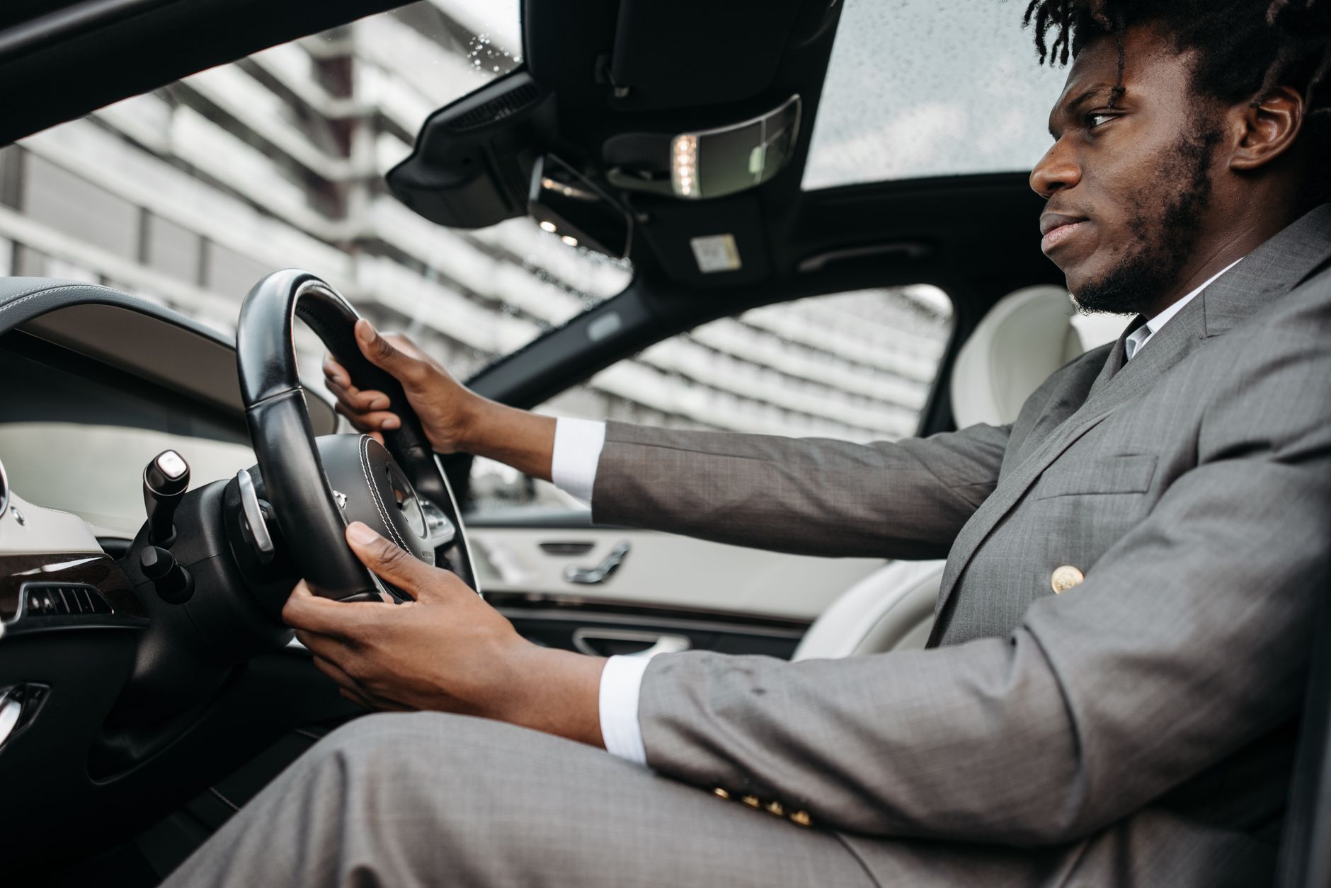 Man in a gray suit driving a luxury car, focused on the road.