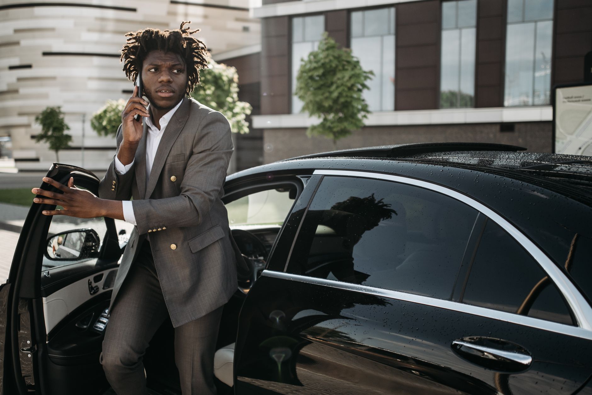 Confident businessman in a suit talking on a smartphone while getting out of a luxury black vehicle.