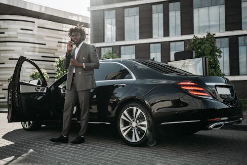 Man in Gray Suit Standing Beside Black Car While Having a Phone Call