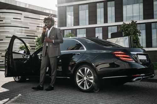 Free Elegantly dressed man in gray suit making phone call next to sleek black car. Stock Photo