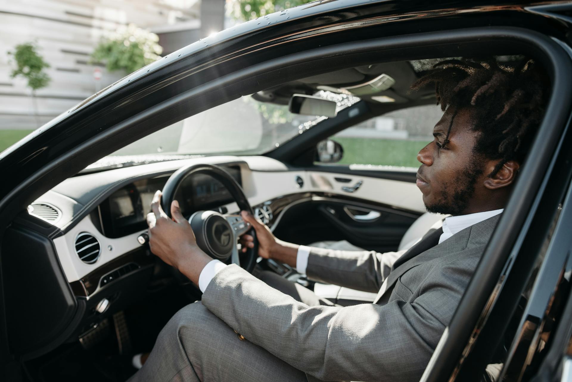 Confident businessman with dreadlocks driving a luxury car in formal attire.