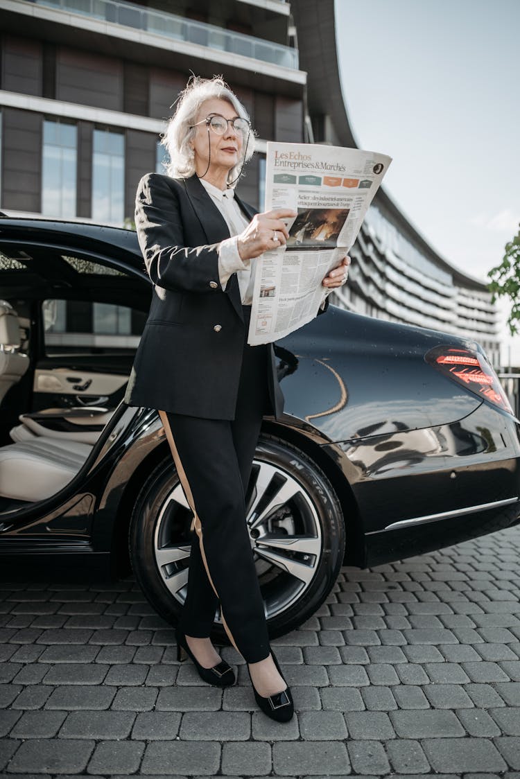 A Woman In Black Suit Reading A Newspaper