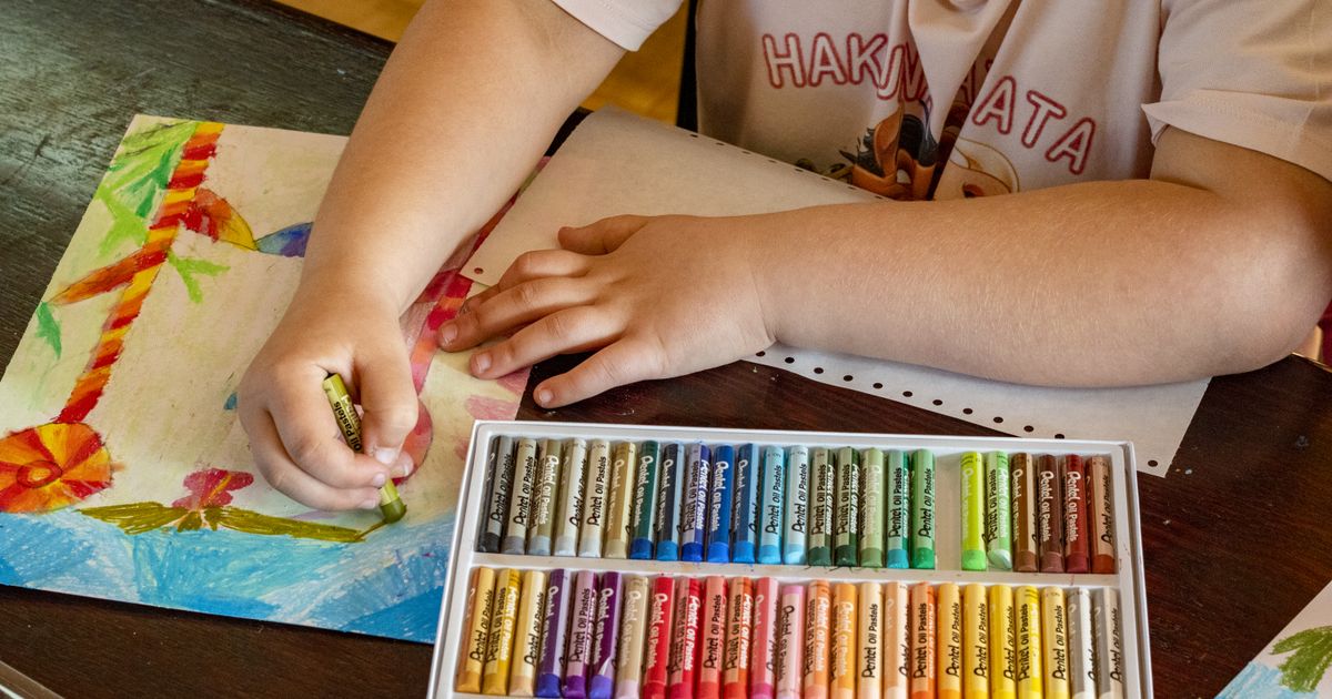 A child drawing with oil pastels from an open box