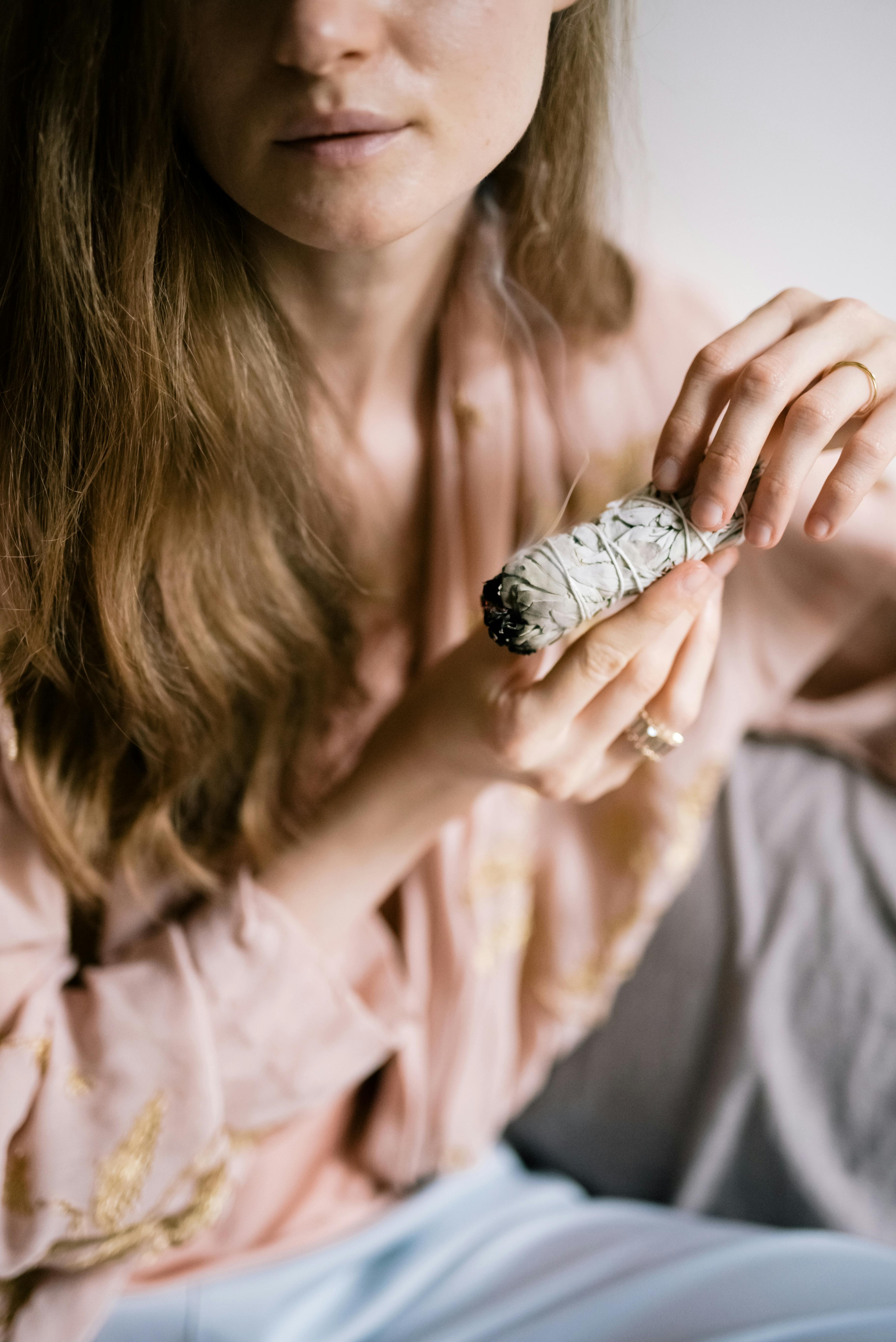 Close-up of a woman holding a burning sage bundle, symbolizing mindfulness and cleansing.