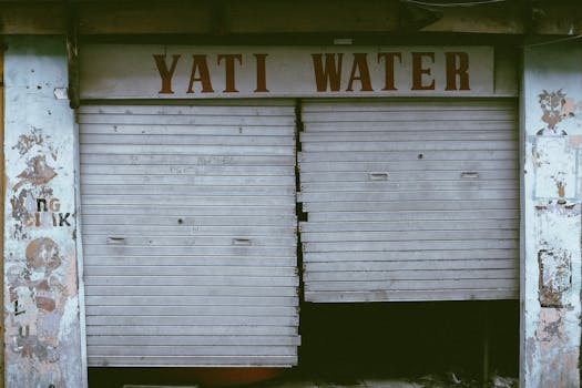 A neglected store entrance with broken roll-up doors and graffiti, showcasing urban decay.