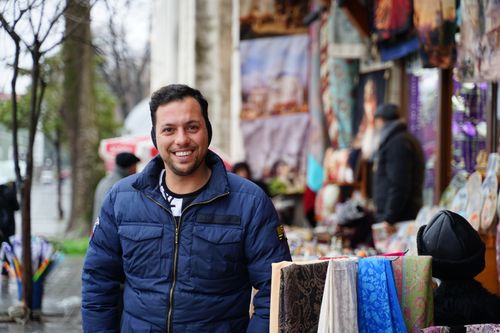 Free A cheerful man wearing a jacket smiles in a vibrant outdoor market atmosphere. Stock Photo
