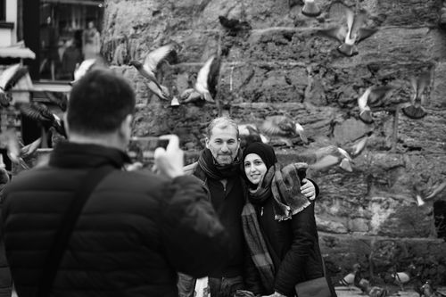 Free A couple poses outdoors with pigeons flying around, captured in a monochrome style. Stock Photo