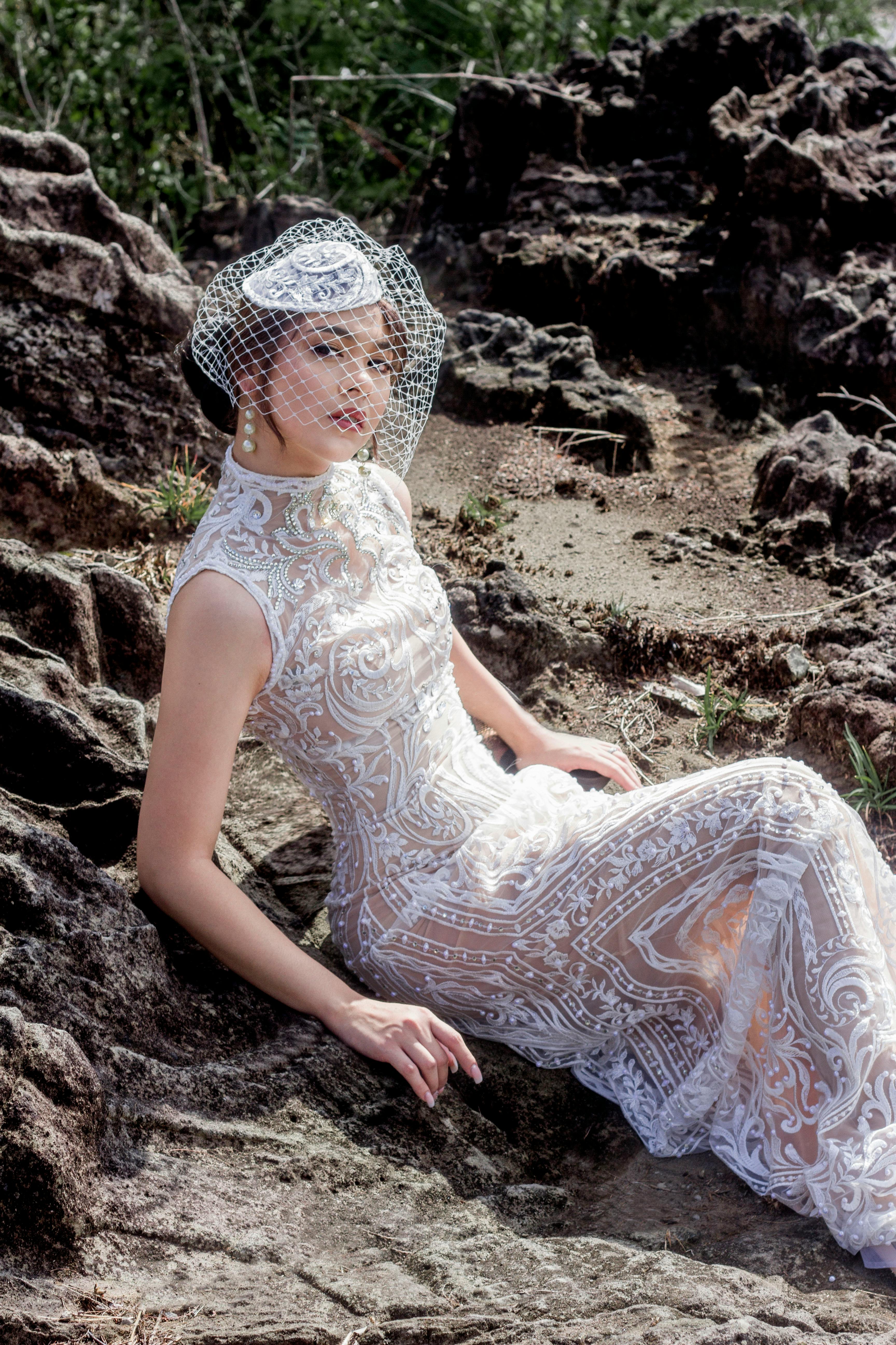 A beautiful bride in a detailed lace wedding gown lounging on rocks, outdoors.