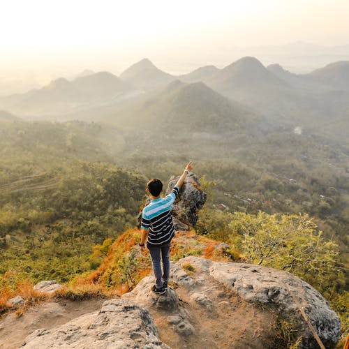 Photo of Man Standing on Rock Mountain Pointing Out Mountain