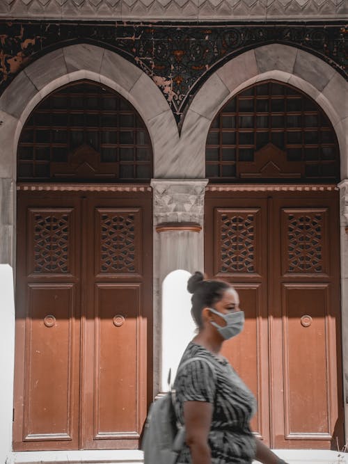 Woman in mask walking past arched building