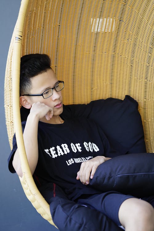 Free Thoughtful Asian teen sitting in wicker hanging chair Stock Photo