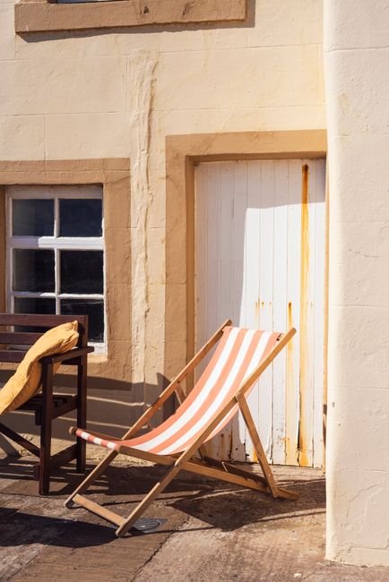 A sunlit deck chair against a rustic cottage wall in Pittenweem, Scotland.