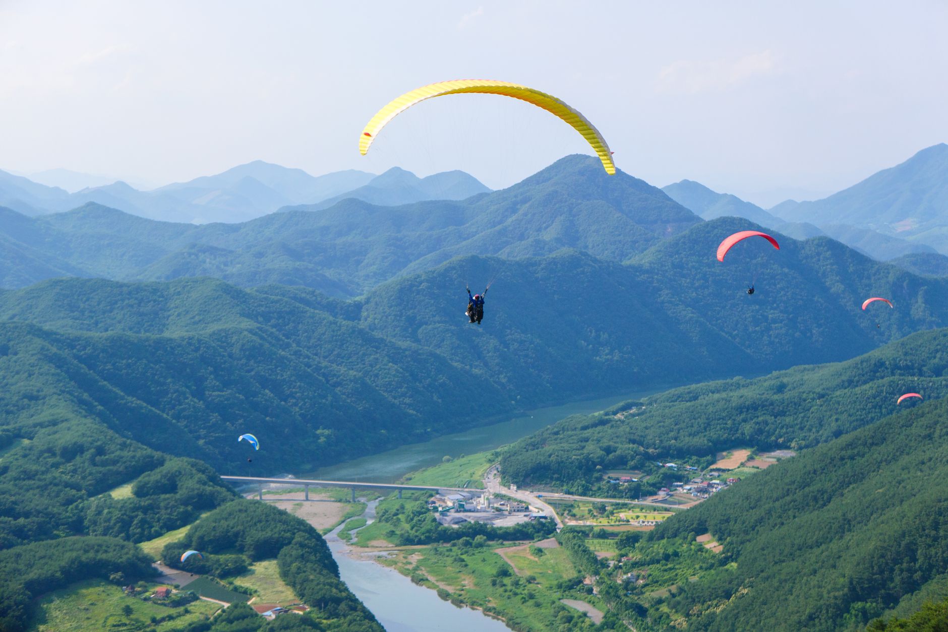 Thrilling paragliding experience with colorful parachutes over stunning green mountain scenery.