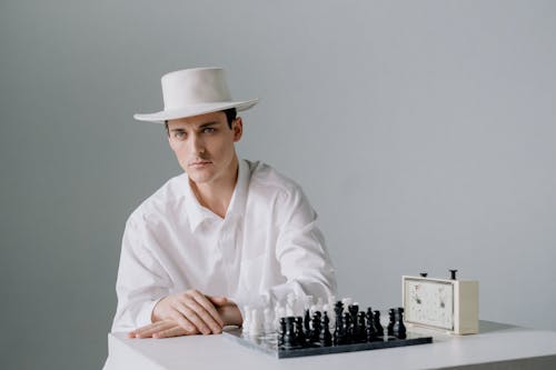 Free Man in White Clothing Sitting in Front of a Chessboard Stock Photo