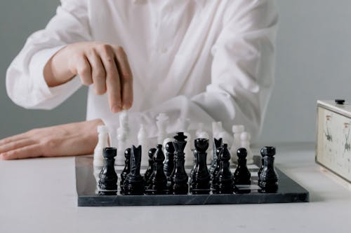 Person in White Long Sleeve Shirt Holding a Chess Piece