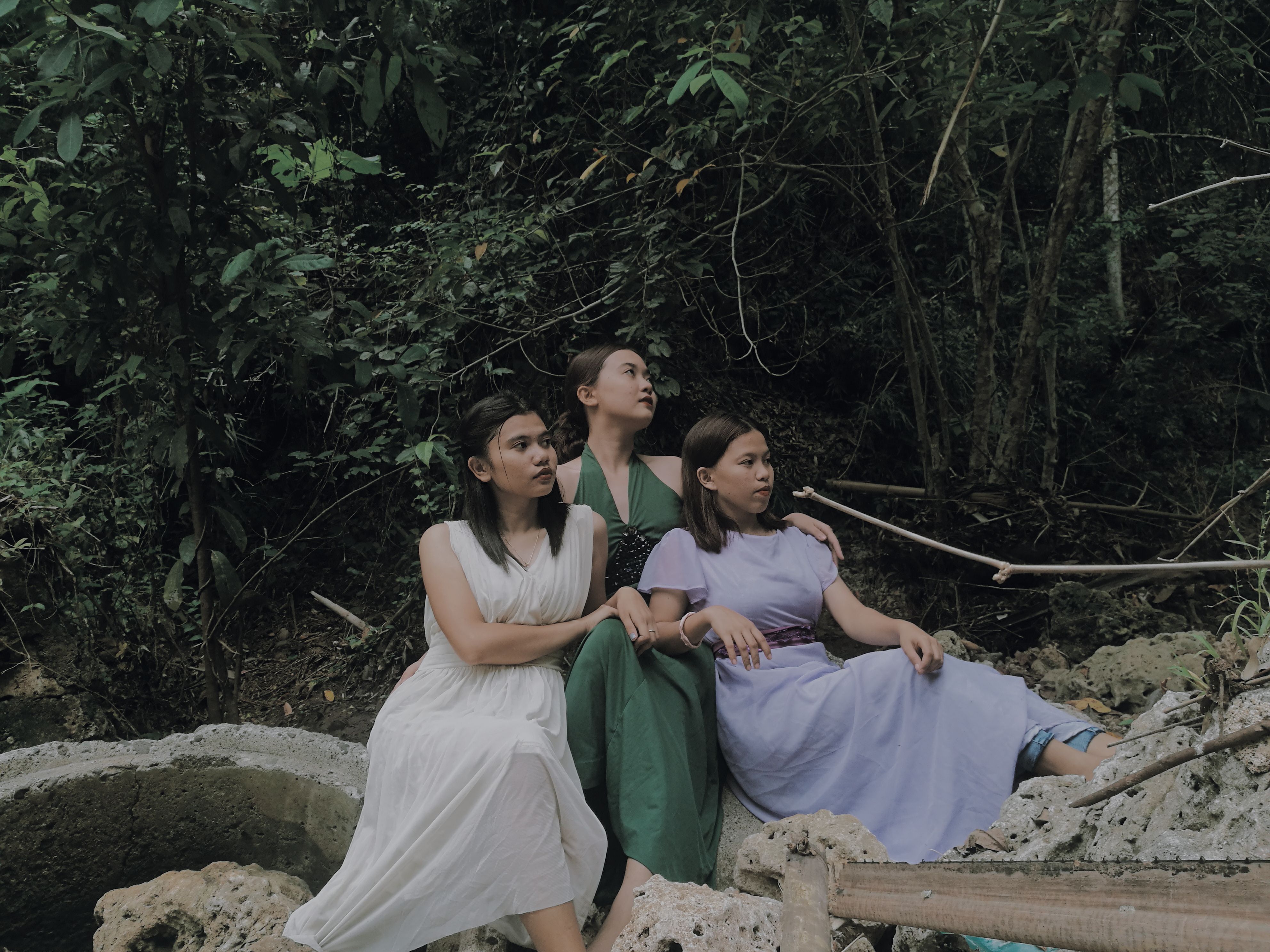 Three women posing serenely in elegant dresses amidst a lush forest in the Philippines.