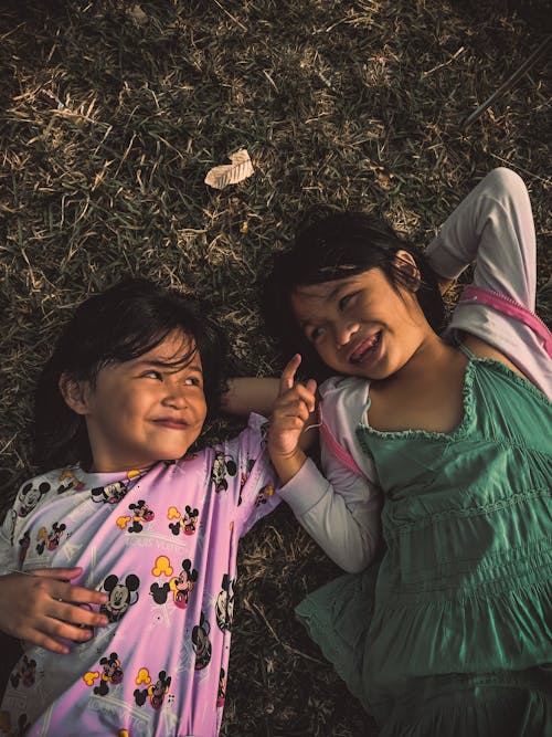 Girls Lying on Grass Field while Happily Looking at Each Other