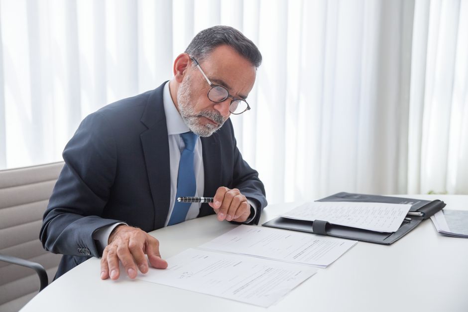 Empresario anciano enfocado en revisar documentos en su escritorio.