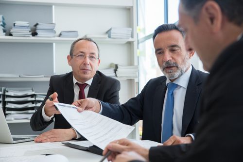 Free Three businessmen discussing documents in a modern office setting. Stock Photo