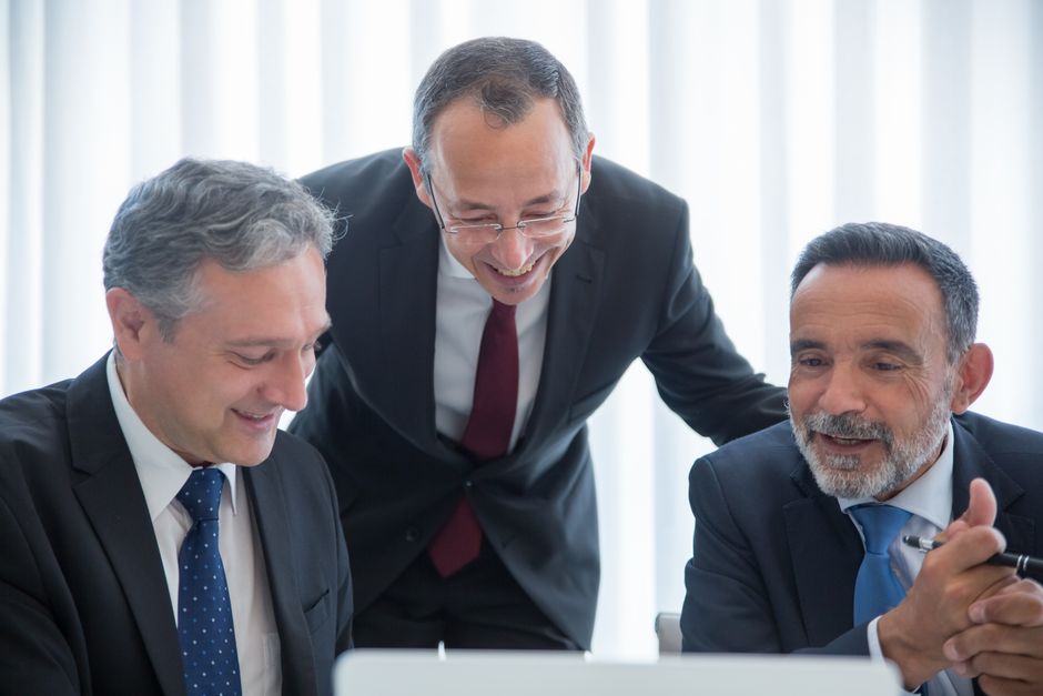 Tres hombres de negocios en trajes, colaborando en equipo en interiores con sonrisas.