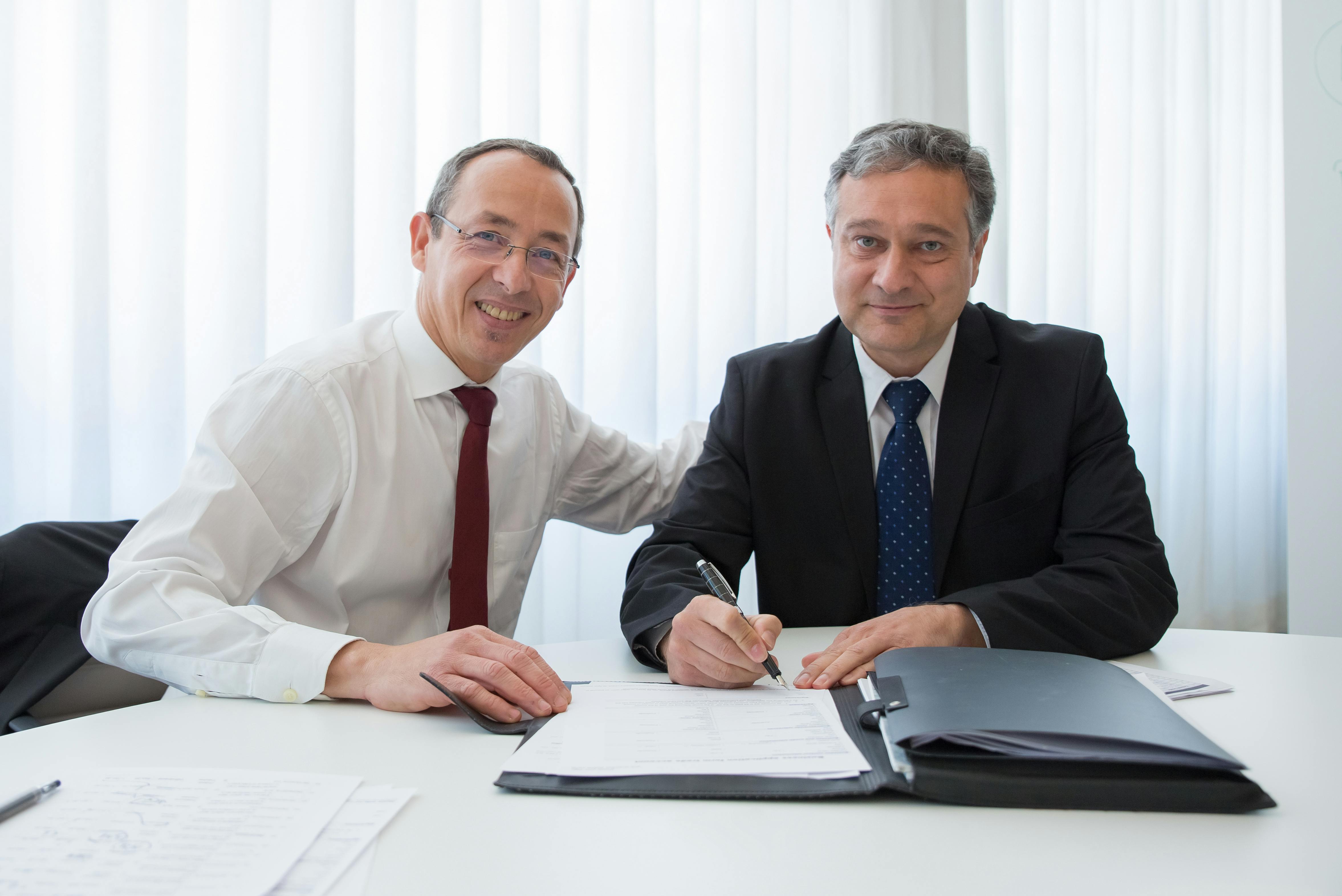 Free A Man in White Long Sleeves Sitting Near the Man in Black Suit Signing Documents Stock Photo