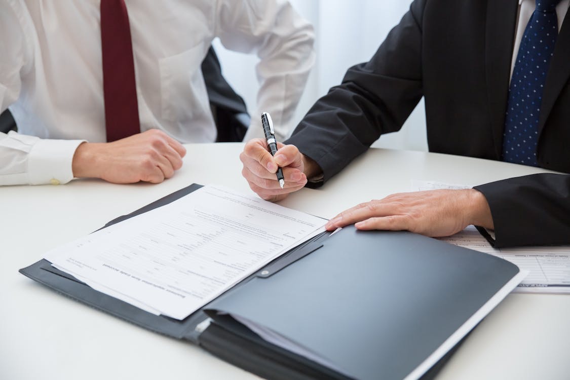 Free A Person in Black Suit Holding a Pen Near the Documents on the Table Stock Photo