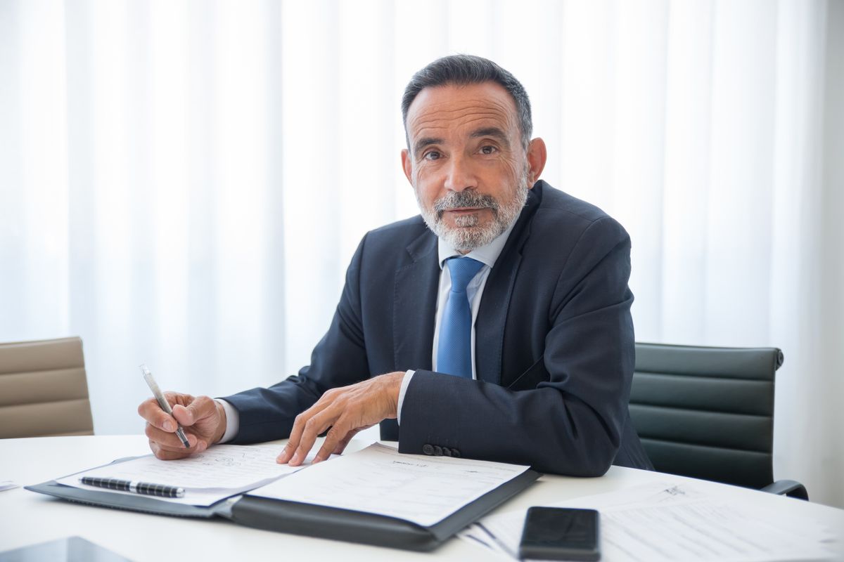 Elderly businessman with a beard signing documents in a modern office setting