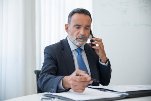 Free A Man in Black Suit Talking on the Phone while Holding a Pen Stock Photo