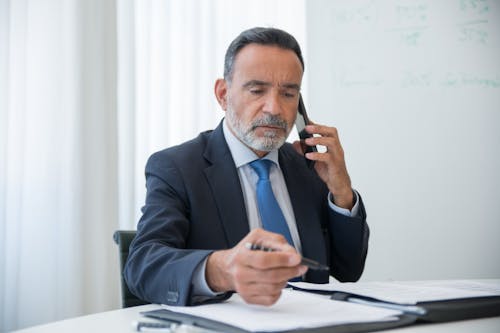 A Man in Black Suit Talking on the Phone while Holding a Pen