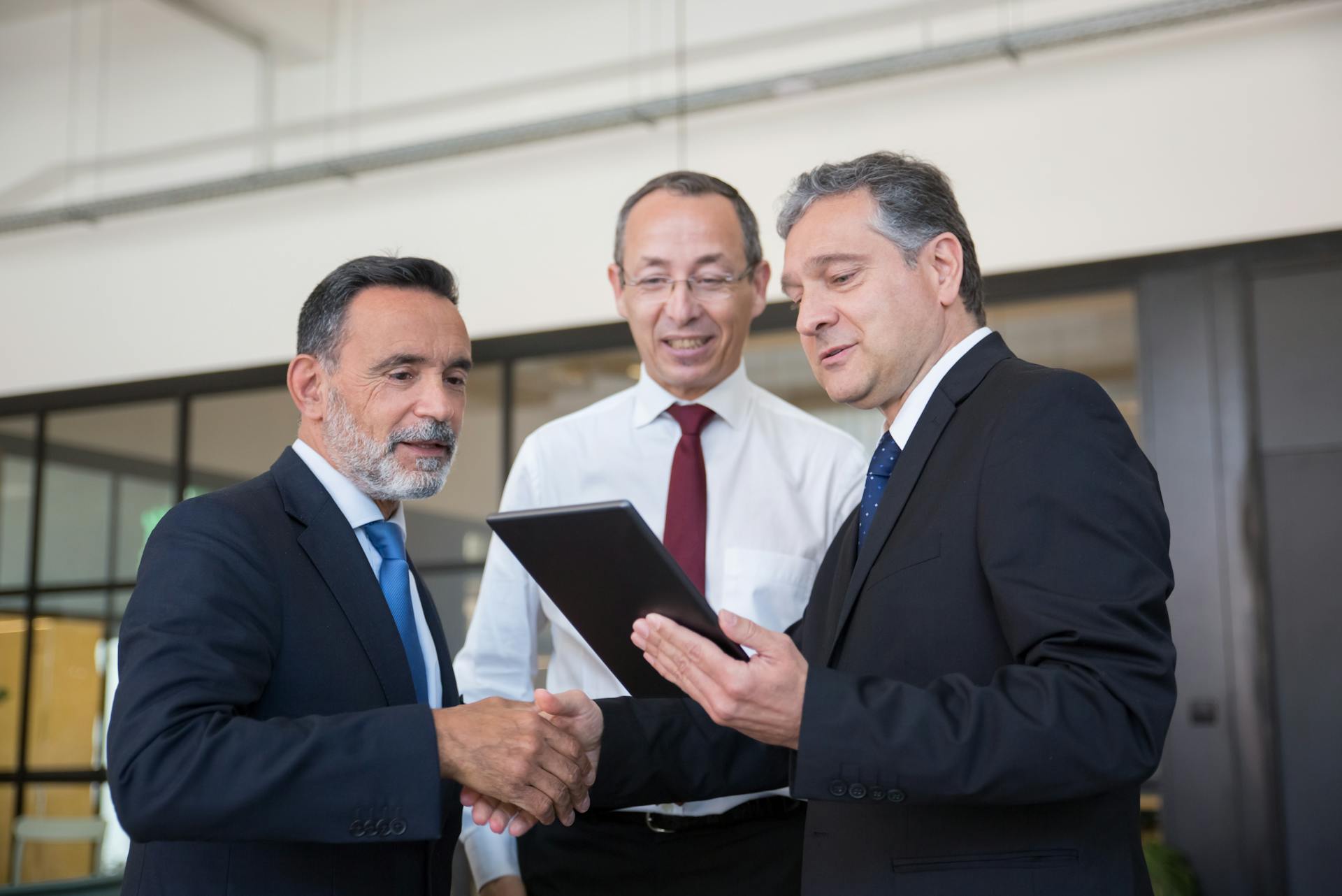 Professional men engaging in teamwork with a digital tablet in a modern office environment.