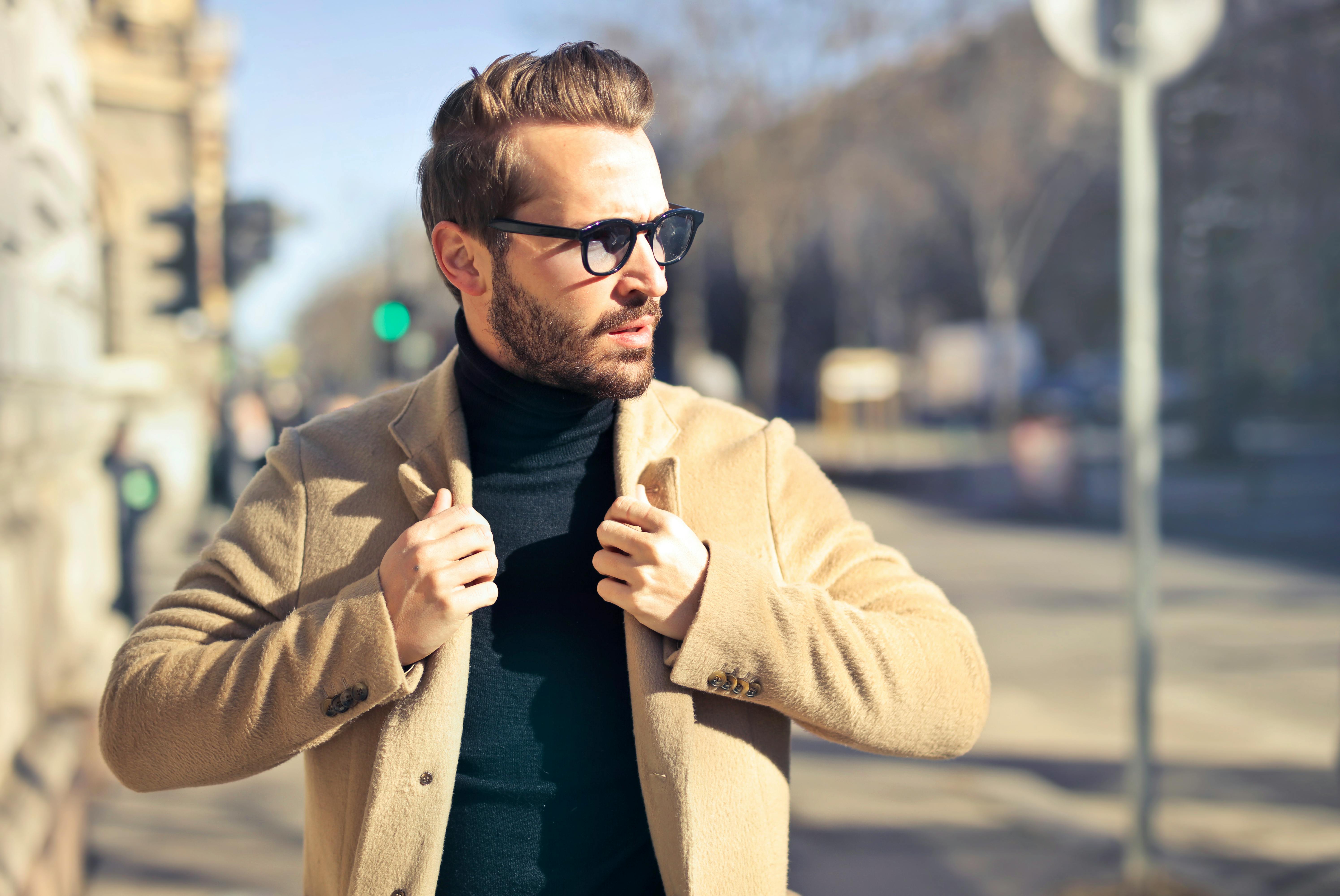 Man wearing eyeglasses and brown jacket outside of the house. | Photo: Pexels