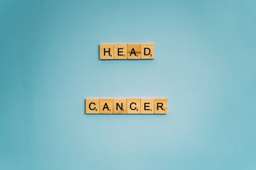 Scrabble tiles spelling 'head cancer' on blue background, promoting awareness.