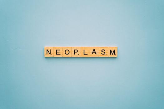 Scrabble tiles arranged to spell 'neoplasm' on a blue surface symbolizing cancer awareness.