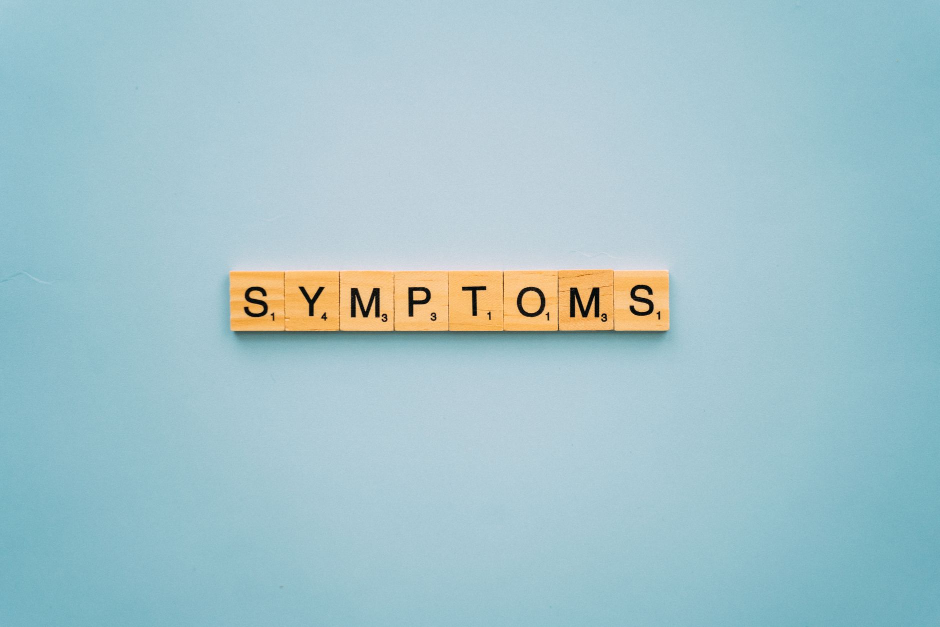 Scrabble tiles spelling 'SYMPTOMS' on a blue background