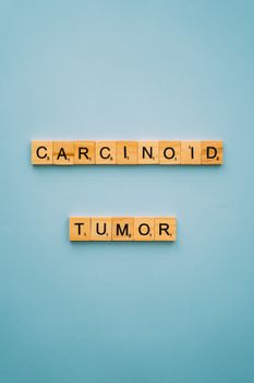 Conceptual cancer awareness image with 'carcinoid tumor' in Scrabble tiles on blue background.