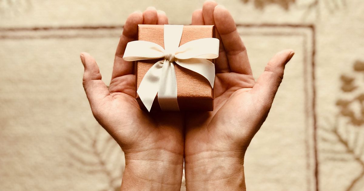 Close up of hands holding a small gift box with a ribbon bow in warm natural light