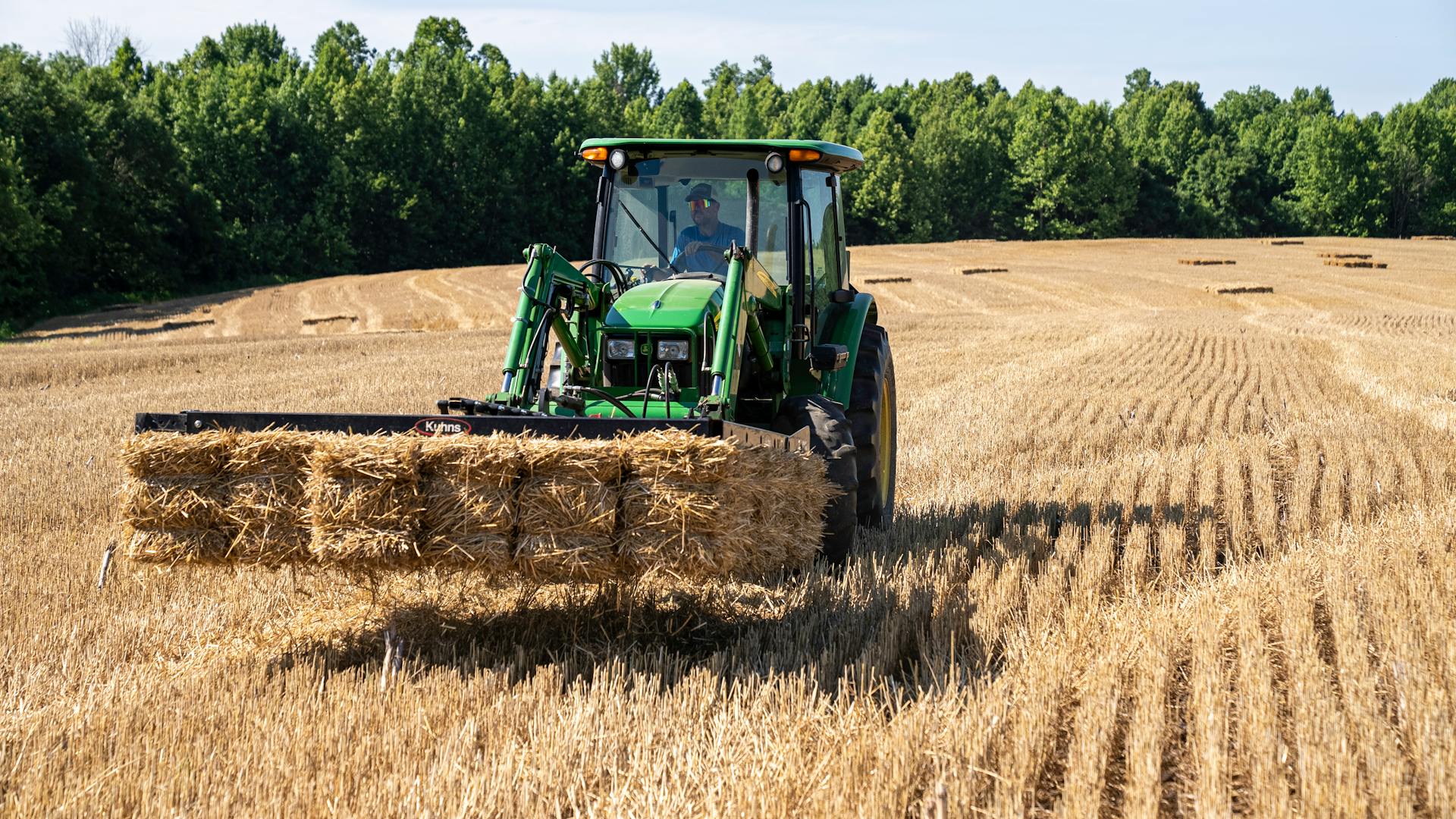 A Farmer Driving Tractor with Baled Hays