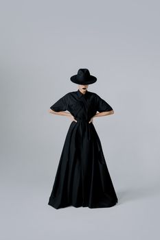 Elegant fashion portrait of a woman wearing a black dress and hat in a studio setting.