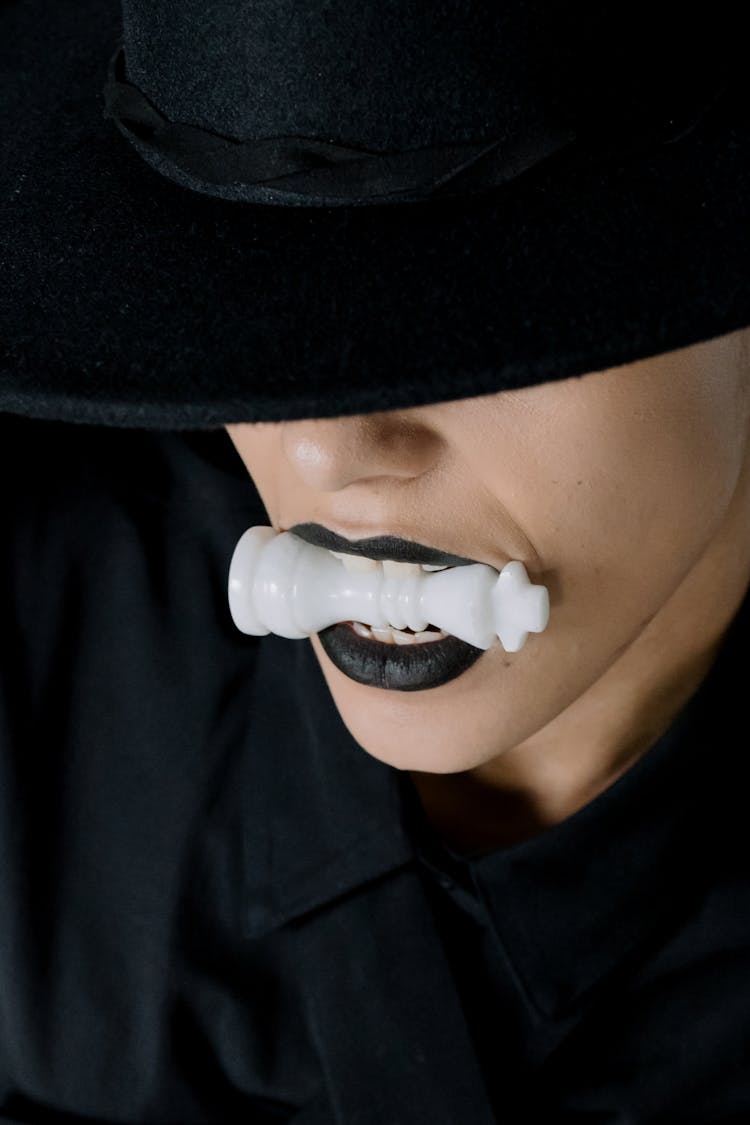 A Person With Black Lipstick Biting A Chess Piece