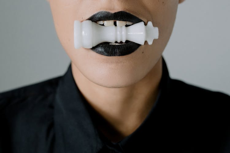 A Person In Black Shirt With Chess Piece On Her Mouth