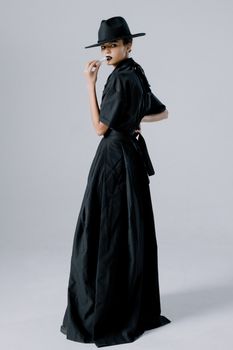 Stylish woman in black attire posing confidently against a minimalistic backdrop.