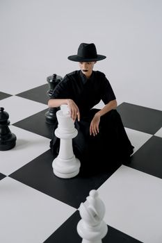 Artistic portrait of a woman in a black dress with a chess theme, evoking elegance and mystery.