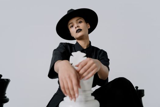 Fashionable woman in black attire posing with large chess piece indoors.