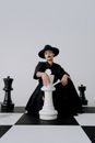 Woman in Black and White Long Sleeve Dress Wearing Black Hat Sitting on Black Chair