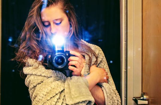 Young woman takes a self-portrait using a DSLR camera in a cozy indoor setting.