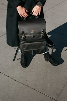 Fashionable black backpack held by a person on a city pavement in daylight.